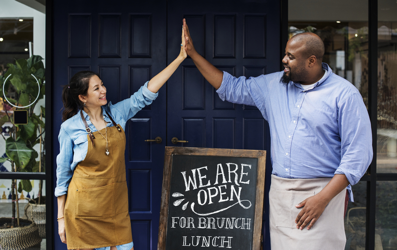 happy small business owners in front of an Open sign